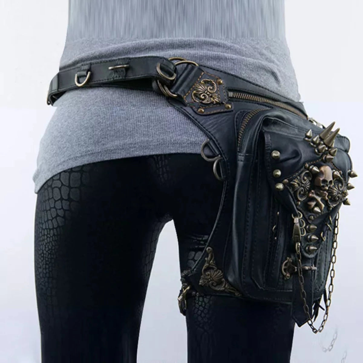 A person is wearing black snake-patterned leggings and a gray sweater, with a Women's Gothic Waist/Hip/Body Fanny Bag featuring spacious compartments, spikes, chains, and gothic-inspired design embellishments.