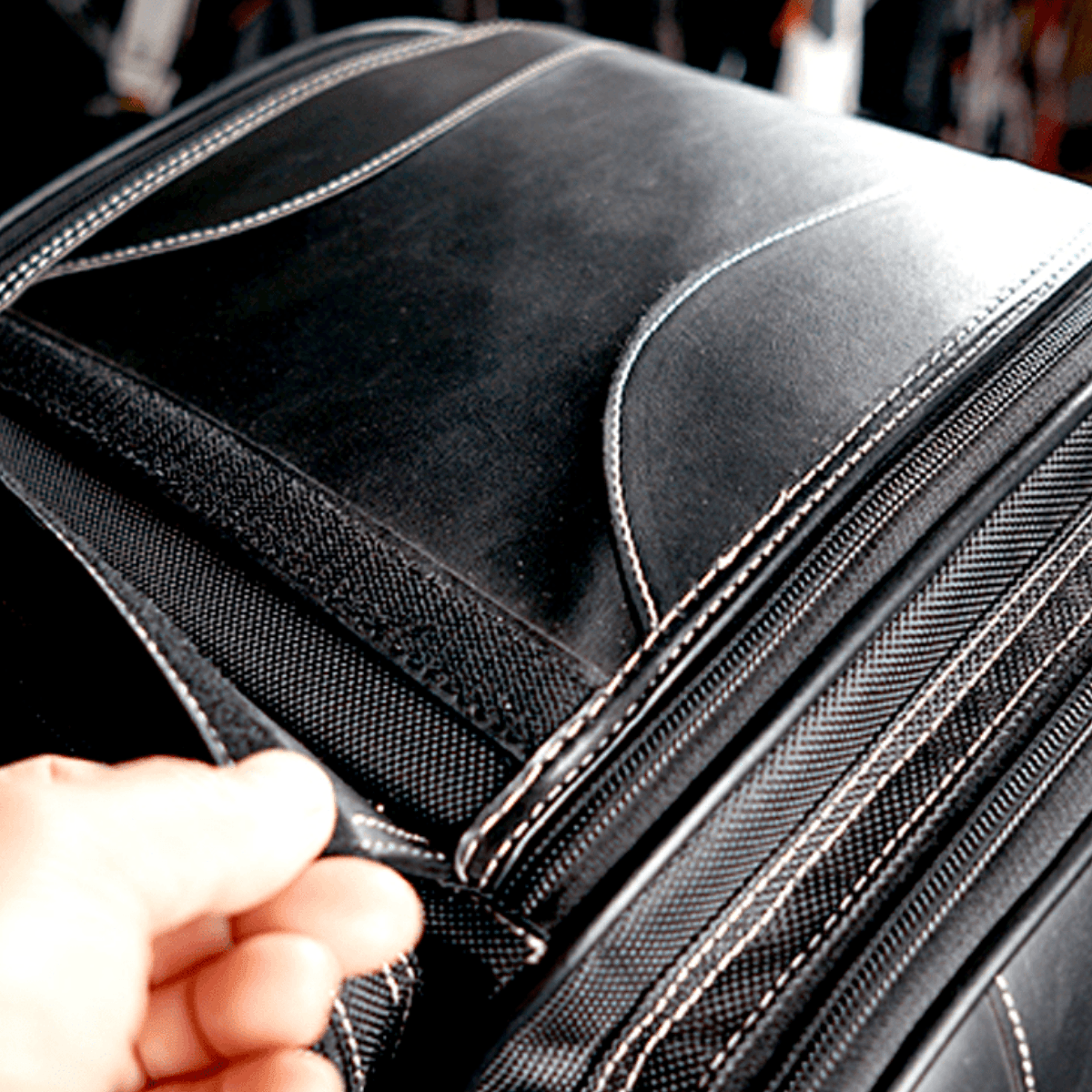 A person is opening the Universal Motorcycle Retro Tail Bag with Waterproof Cover made of waterproof leather and fiber material.