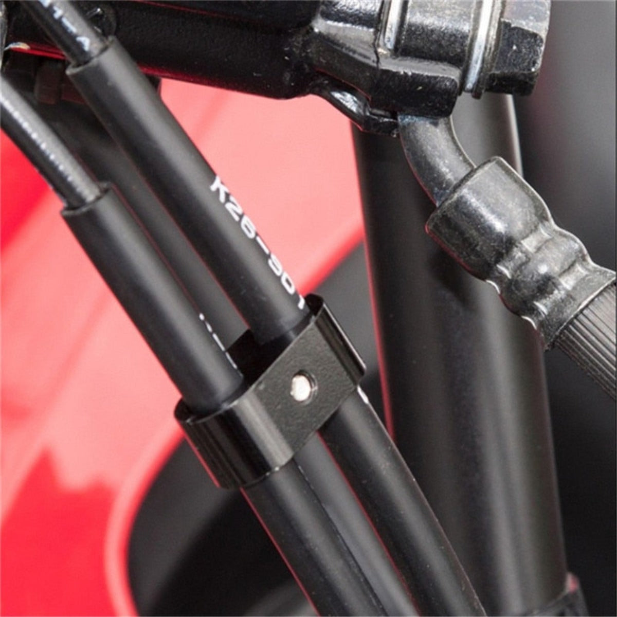 Close-up of black cables held together by a Universal Motorcycle Brake Throttle Cable Clip Clamp Holder with a visible screw, against a background that includes a red and black surface.