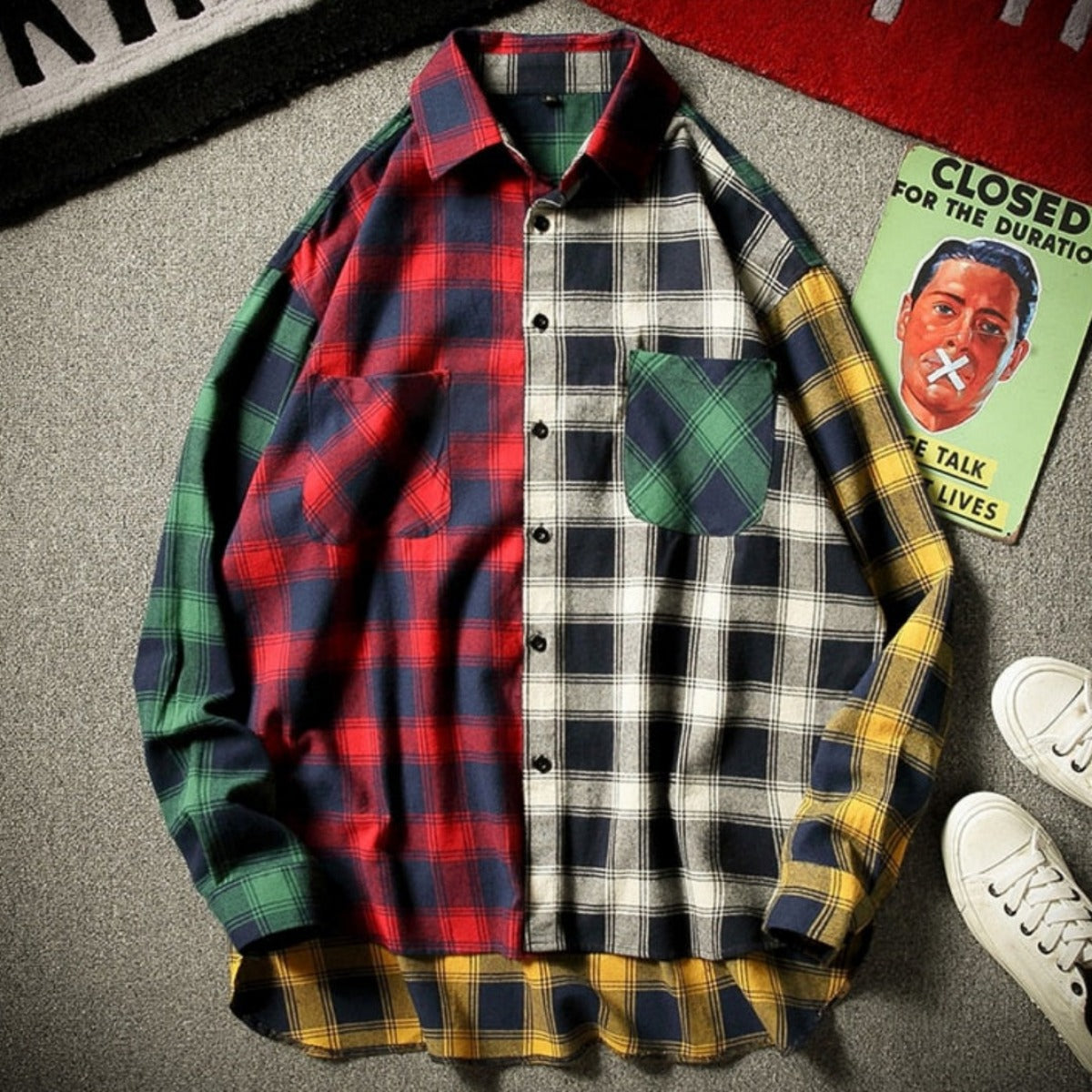 A Men's Finest Blended Color Flannel Shirt in red, featuring a variety of patterns including green, blue, yellow, and gray sections, is displayed on a textured surface alongside white sneakers and a closed book. Ideal for individuals who value stylish men's apparel with classic flair.