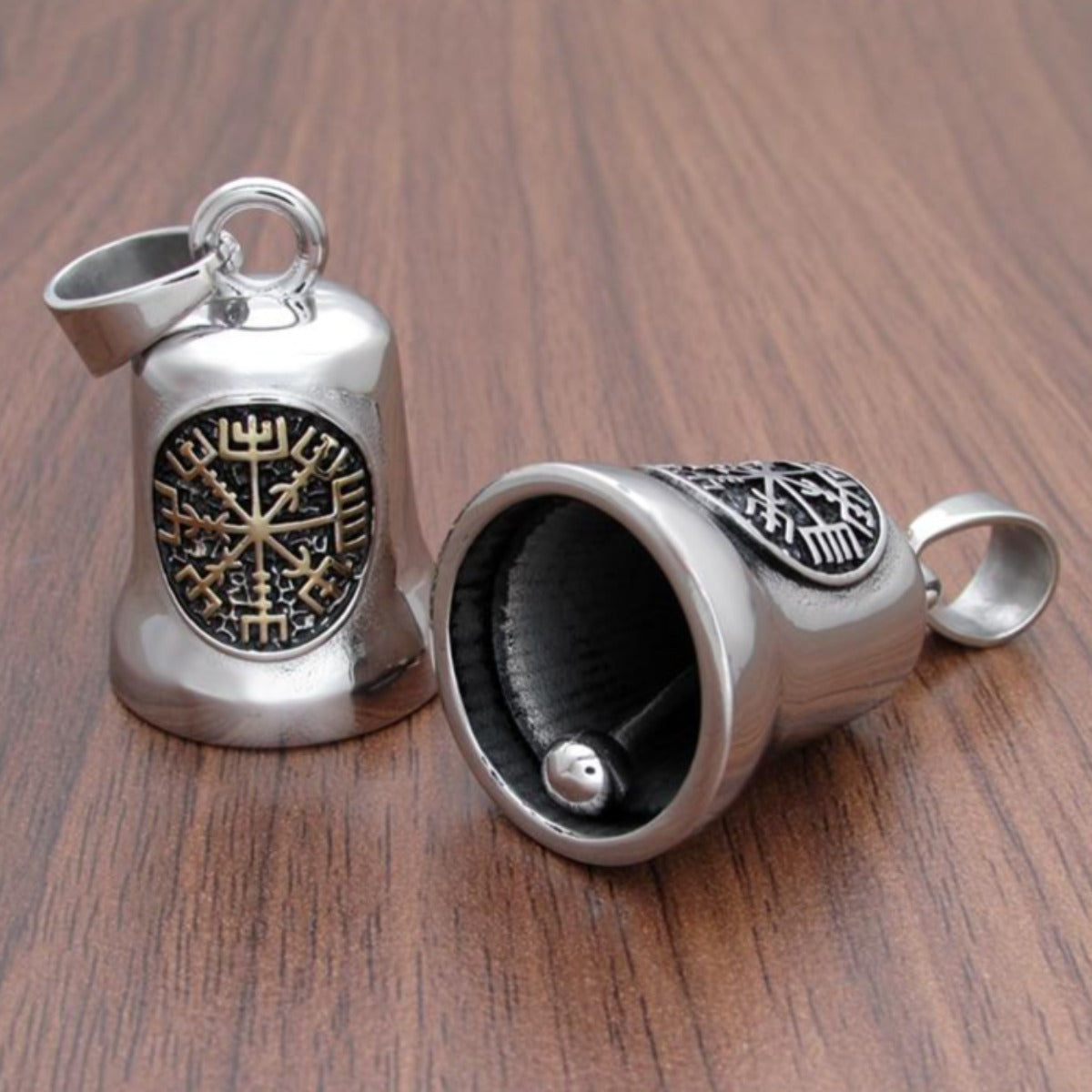 Two Stainless Steel Viking Compass Gremlin Bell pendants with Norse symbols lying on a wooden surface, one open to reveal a hidden compartment.