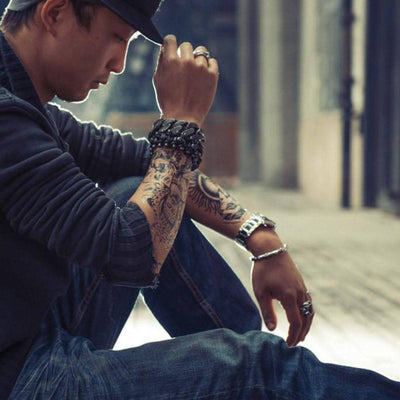 A freedom rider with tattoos, sporting a biker styling item - the Skeleton Chain Buckle Bracelet - sitting on the ground.