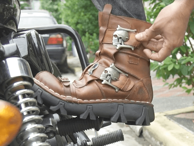 A person is putting on a pair of Handmade Leather Skull Boots.