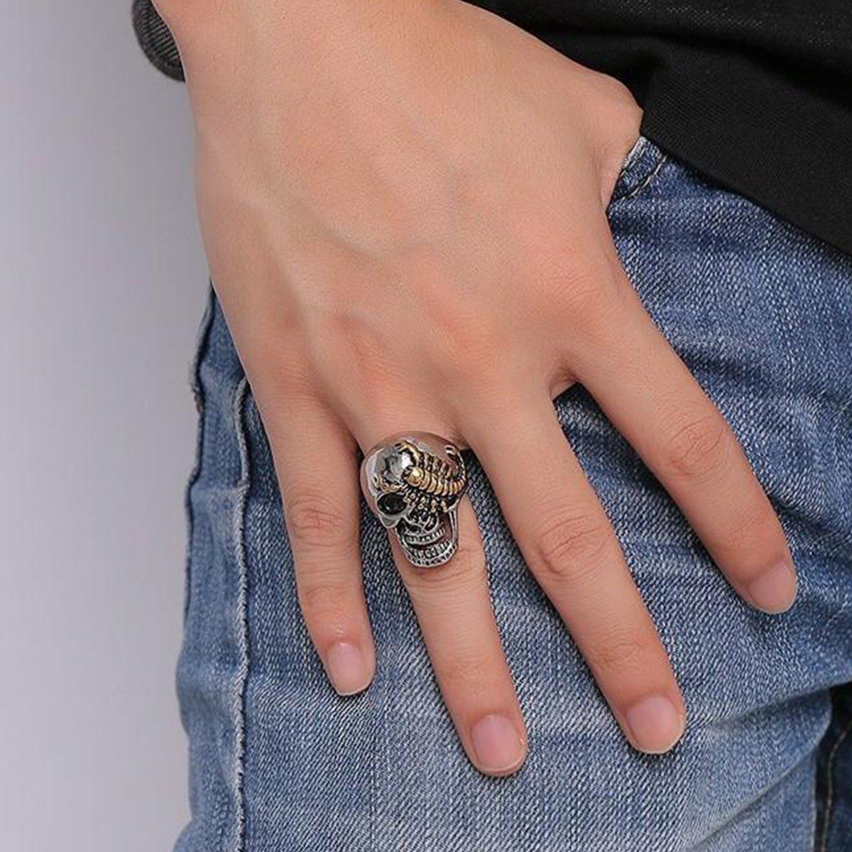 A hand with a personalized Stainless Steel Punk Rock Silver Skull & Gold Scorpion Ring on the middle finger, resting on the hip of blue denim jeans.