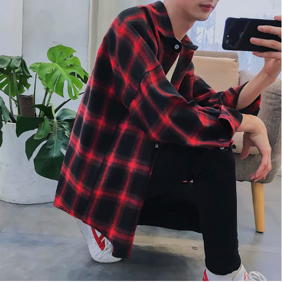 A person crouches indoors, capturing a mirror selfie while wearing a Men's Classic Plaid Flannel Shirt in red and black, paired with black pants and white sneakers. In the background, a potted plant adds a touch of nature to the scene.