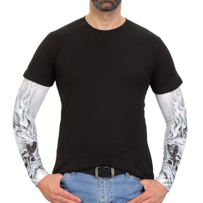 Man wearing a black t-shirt, blue jeans, a black belt, and Hot Leathers Assassin Arm Sleeve with skull and flame designs, standing with hands in pockets against a plain background.