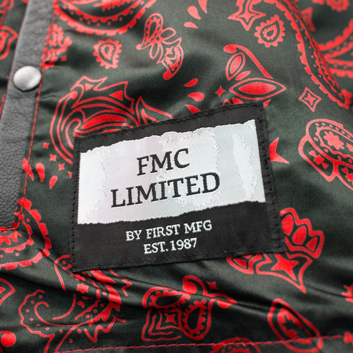 Close-up of a label saying "FMC Limited by First MFG Est. 1987" on a First Manufacturing Men's The Cut Motorcycle Leather Vest, Black/Red featuring red and green paisley milled cowhide fabric.