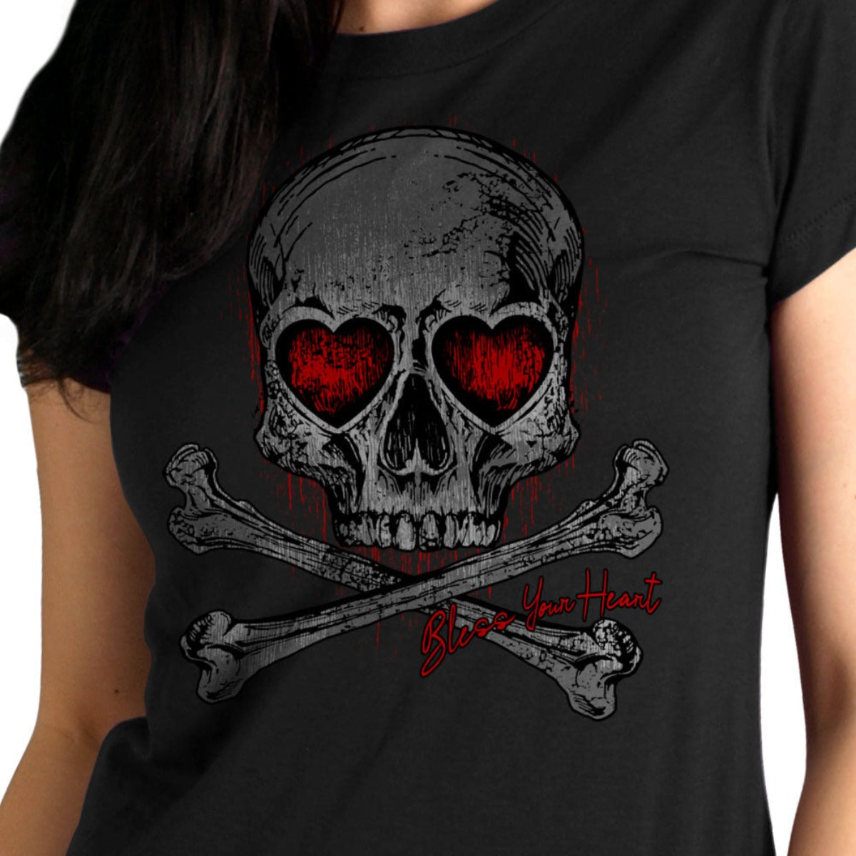 A woman wearing the Hot Leathers Ladies Heart Eyes Skull T-Shirt, a screen-printed black cotton tee showcasing a skull and crossbones design. The skull features heart-shaped eye sockets with the whimsical text "Bless Your Heart" underneath. Crafted in the USA, this casual T-shirt combines style and comfort seamlessly.