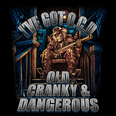 A skeleton in a hat and coat with a rifle relaxes on a porch, displaying skeleton artwork. The text reads "I've Got O.C.D.: Old Cranky & Dangerous" on this black, 100% cotton men's t-shirt from Hot Leathers.