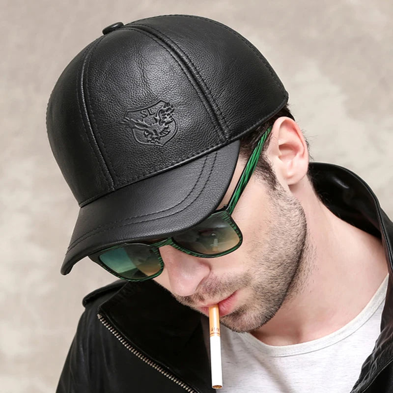 A person, donning the ALR™ Genuine Leather Eagle Baseball Cap in genuine black cowhide, pairs it with sunglasses and a sleek black jacket. The adjustable cap size enhances its versatility, completing an edgy look as a cigarette hangs casually from their mouth.