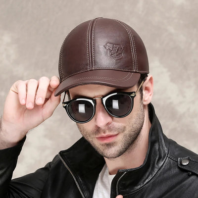 Wearing an ALR™ Genuine Leather Eagle Baseball Cap, adjustable in size and brown, paired with sunglasses, a person adjusts the cap using their left hand while sporting a black cowhide jacket for an effortlessly cool look.