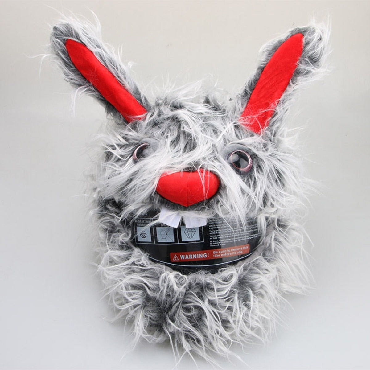 A Cool Motorcycle Helmet Cover - Gray Bunny with large red ears, bulging eyes, a red nose, and prominent white teeth. This attention-grabbing accessory also features a warning label attached below the chin area.