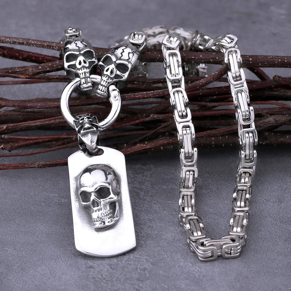 The ALR™ Stainless Steel Pirate Skull Pendant Necklace, featuring a silver design and intricate chain, is artfully set against a wooden branch background.