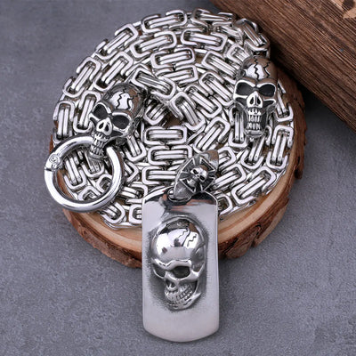 On a wooden surface, the ALR™ Stainless Steel Pirate Skull Pendant Necklace features a silver chain with intricate skull designs and a striking stainless steel pendant. Its vintage appeal adds timeless charm to any collection.