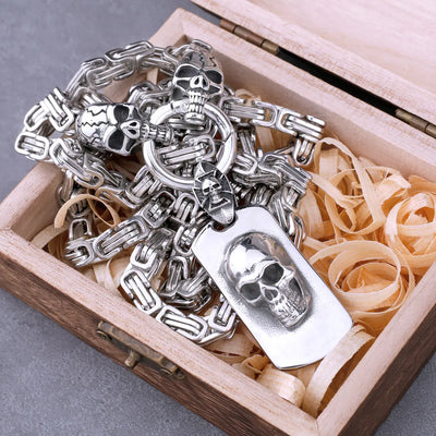 The ALR™ Stainless Steel Pirate Skull Pendant Necklace, featuring a silver skull chain and tag, comes packaged in a wooden box with straw filling, evoking the charm of vintage jewelry.