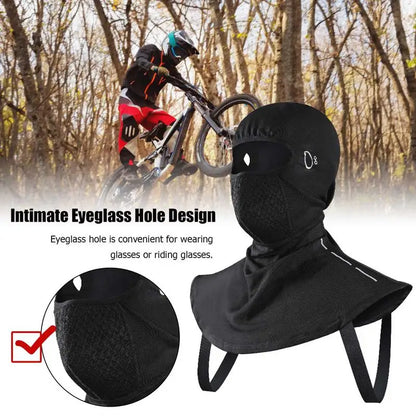 A cyclist wearing a helmet rides a mountain bike through the woods. In the foreground, an ALR™ Winter Balaclava Neck Warmer with an eyeglass hole lies ready, doubling as a neck warmer—a versatile winter sports accessory.
