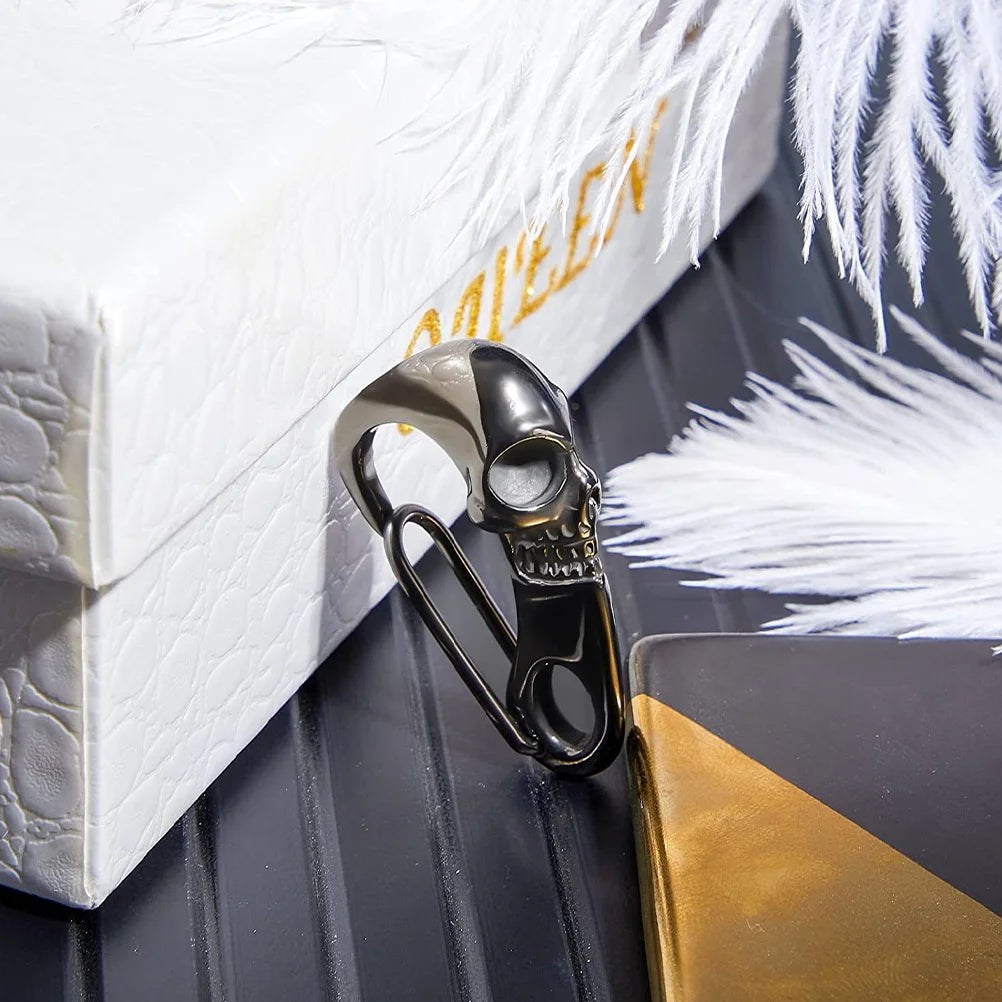 The ALR™ Skull Keychain Carabiner, a Gothic-inspired skull-shaped stainless steel bottle opener, sits beside a white box with gold text and decorative white feathers, adding an edgy touch to any collection.