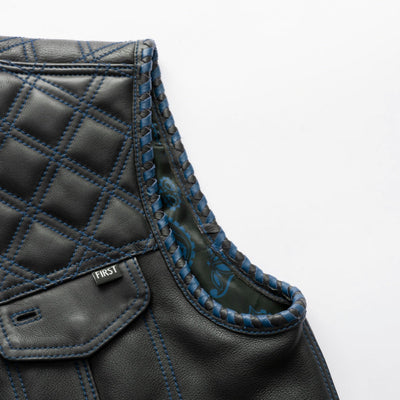 Close-up of the First Manufacturing Sinister Men's Motorcycle Leather Vest in black and blue, showcasing blue-stitched quilting and decorative edge trim, a small detail tag labeled "First," and a concealed carry pocket.