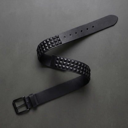 Pyramid studded belt laid in an S curve on dark concrete seen from above
