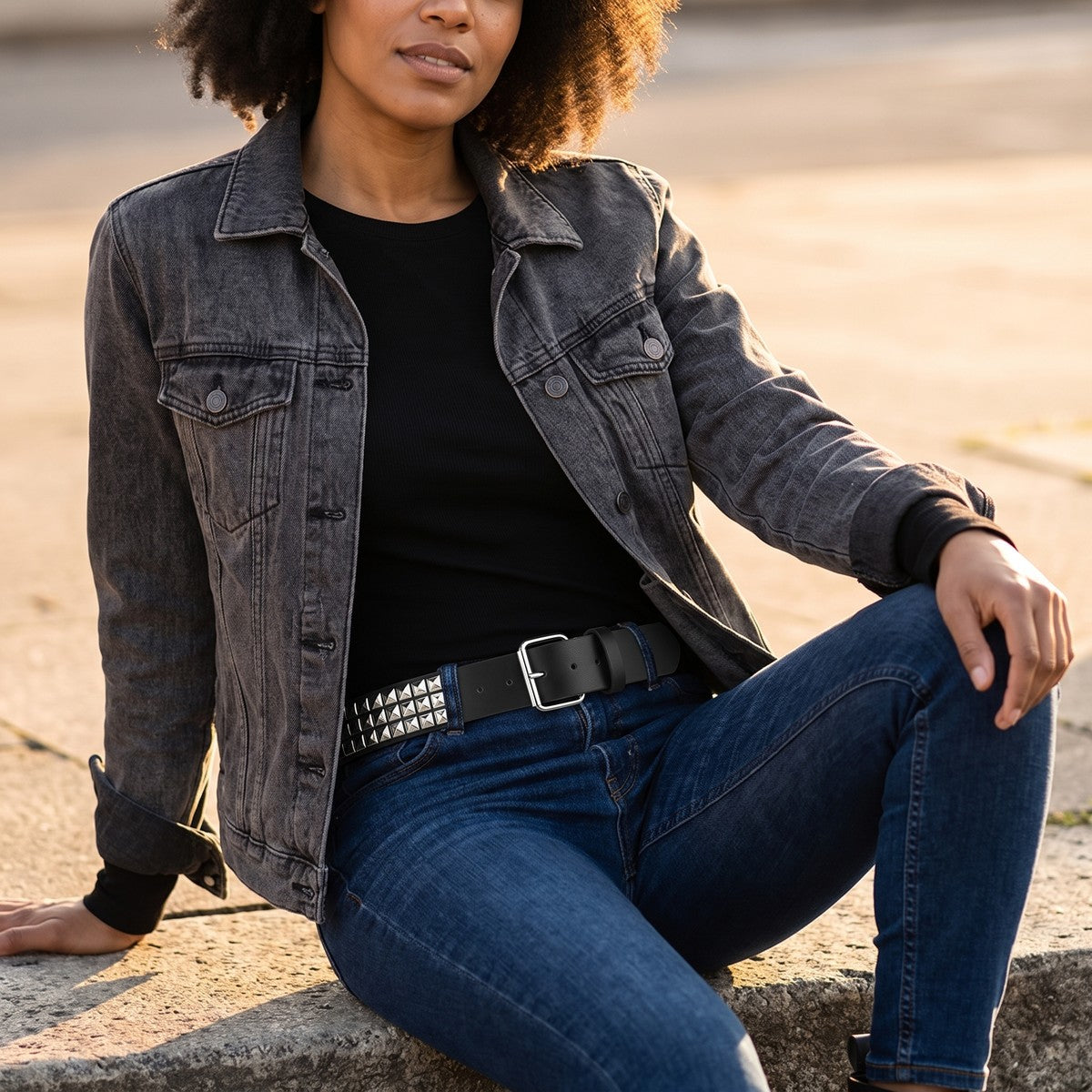 Woman seated on a step wearing the pyramid studded belt with a denim jacket