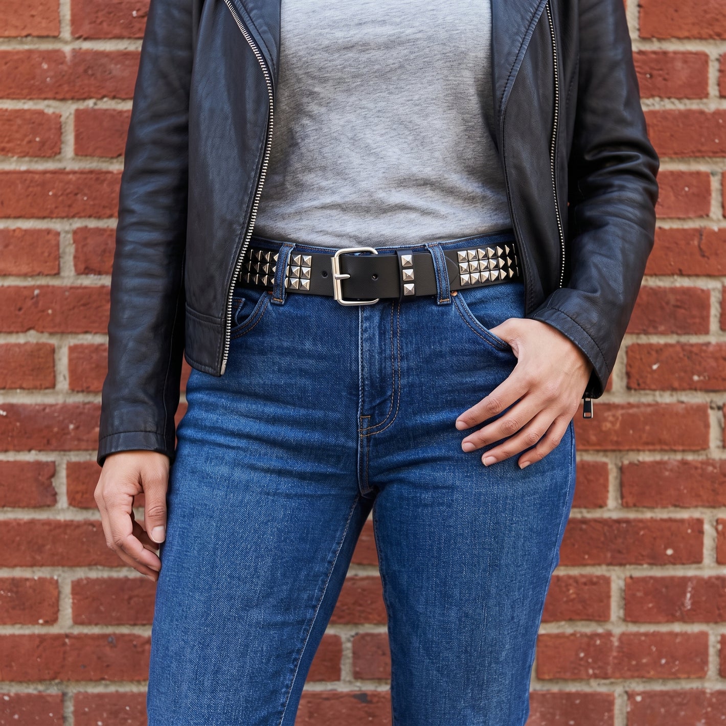 Woman wearing the pyramid studded belt through the loops of blue jeans with a leather jacket