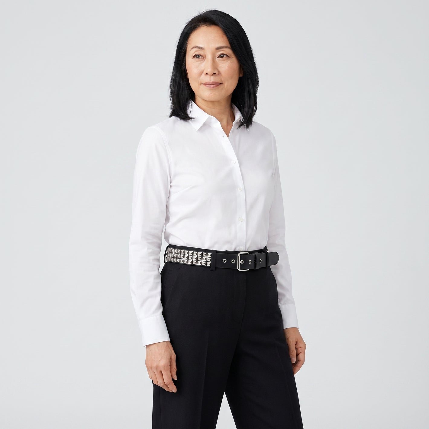 Woman wearing the silver pyramid studded belt with high waisted black trousers and a white shirt