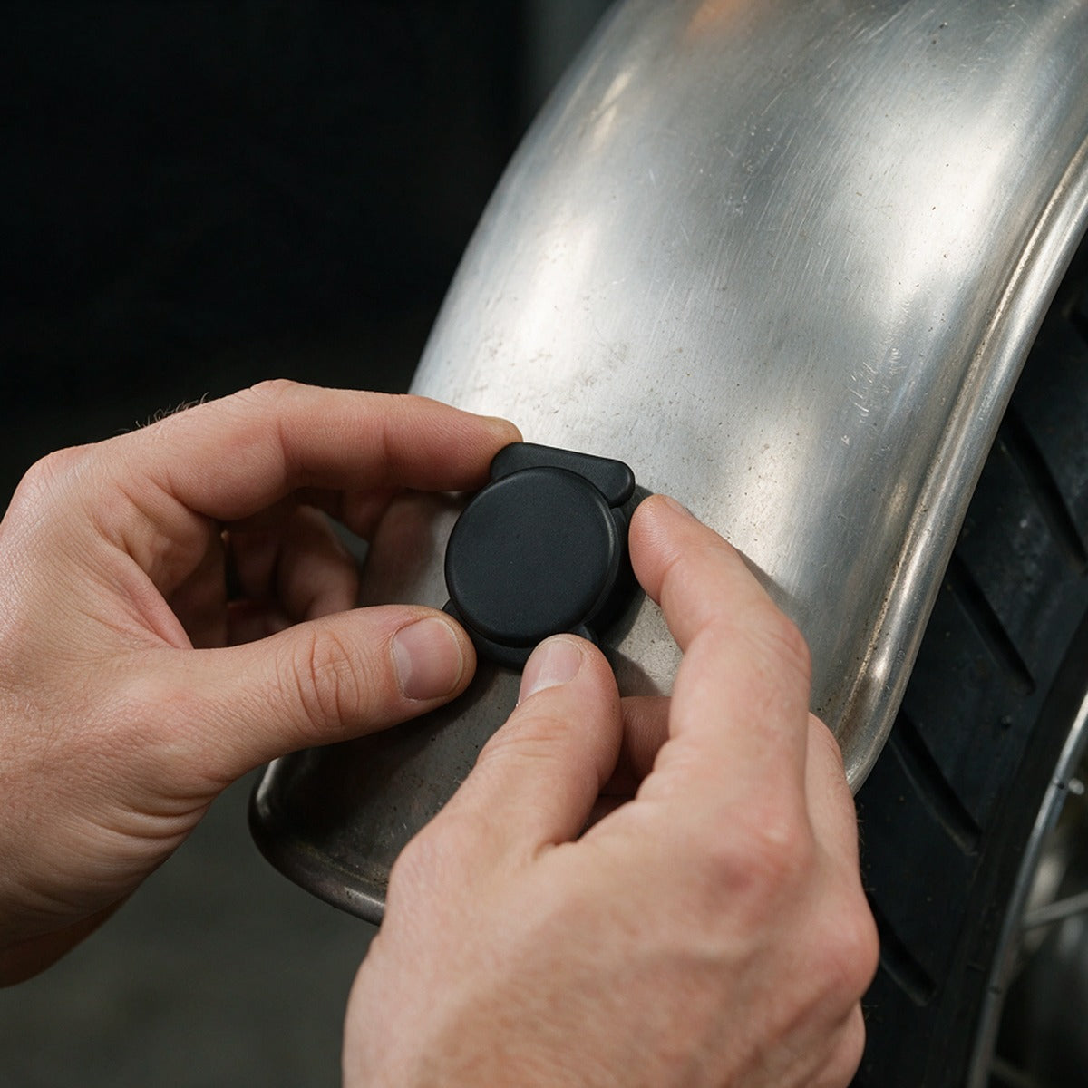 Hands pressing the magnetic Bluetooth finder tag onto a motorcycle fender