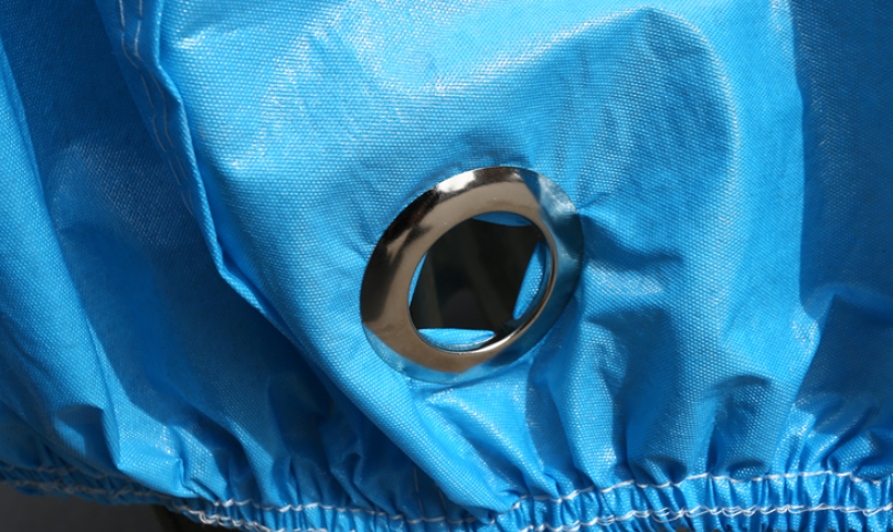 A close-up of a waterproof blue fabric, commonly used in motorcycle covers, featuring a metal eyelet. The Protective Oxford Cloth Motorcycle Cover is gathered and elasticized at the bottom edge.