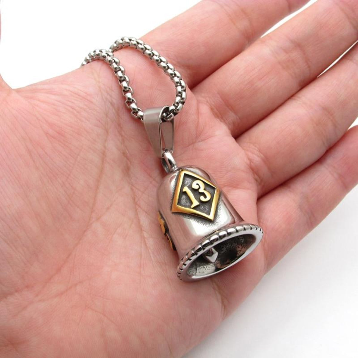 A person is holding a stainless steel Lucky 13 Gremlin Bell necklace.