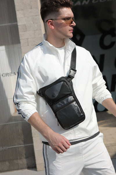 A person in a white tracksuit and sunglasses strolls outside, showcasing the Men's Multi-Function Chest/Waist Bag in black as a versatile accessory.