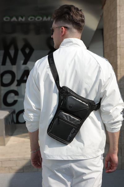 A man in a white jacket and pants stands before a building with partially visible window text, sporting the versatile Men's Multi-Function Chest/Waist Bag.