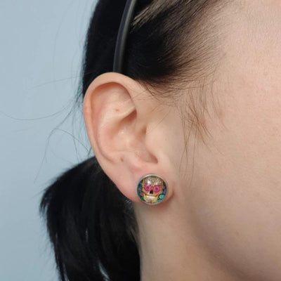 A woman's ear adorned with vibrant Sugar Skull Stud Earrings - a striking statement jewelry piece.