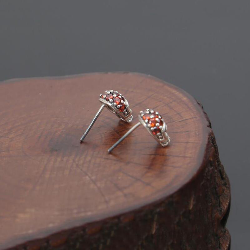 A pair of Fashion Skull Stud Earrings with red stones on top of a piece of wood.