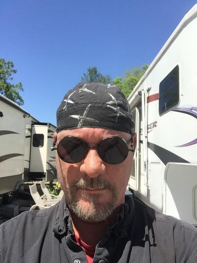 A man wearing Rebel Sunglasses and a bandana in front of an rv.