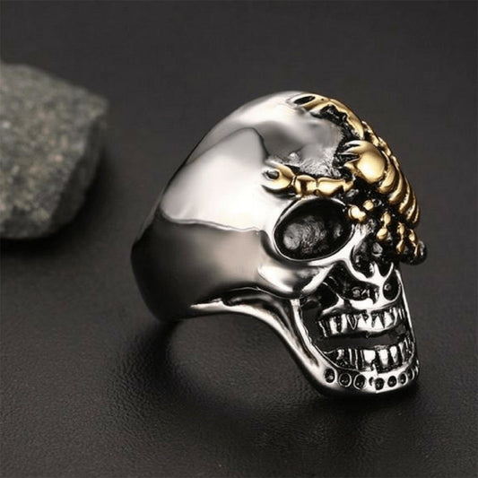 The **Stainless Steel Punk Rock Silver Skull & Gold Scorpion Ring** is showcased on a black surface with a small stone beside it, highlighting its handcrafted design featuring a silver skull adorned with a gold scorpion on the forehead.