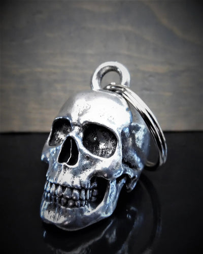 A close-up of a Daniel Smart Skull Guardian Bell crafted from lead-free pewter, with a dark background. The skull has intricate detailing, and the keyring loop is visible at the top. Comes packaged in a sleek velveteen drawstring bag for an added touch of elegance.