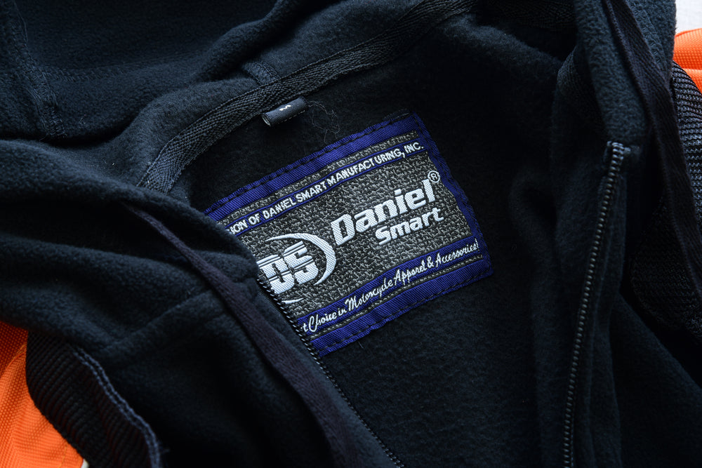 Close-up of a Daniel Smart Women's Mesh 3-in-1 Riding Jacket (Black/Orange) label on a black garment.