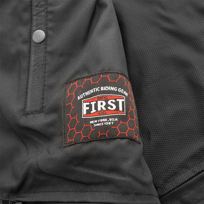 A close up of a black jacket with a logo on it, showcasing its First Manufacturing Upside Leather Vest design.