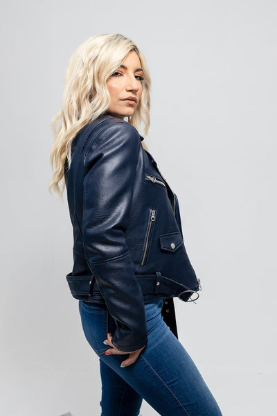Woman with blond hair wearing a First Manufacturing Remy - Women's Vegan Faux Leather Jacket in navy blue with an asymmetrical zipper and jeans, looking over her shoulder.